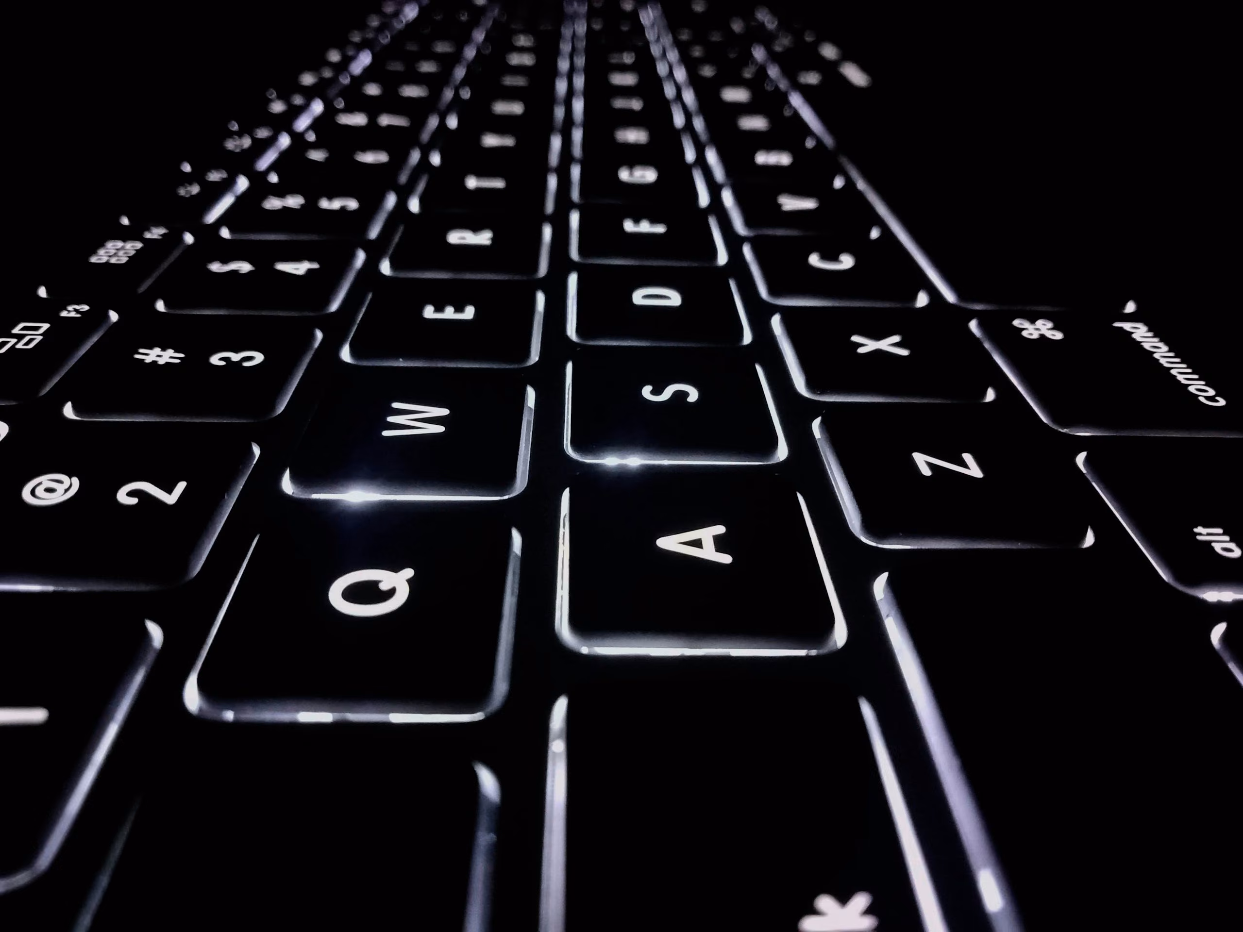 Close-up of a backlit black laptop keyboard in a dark room