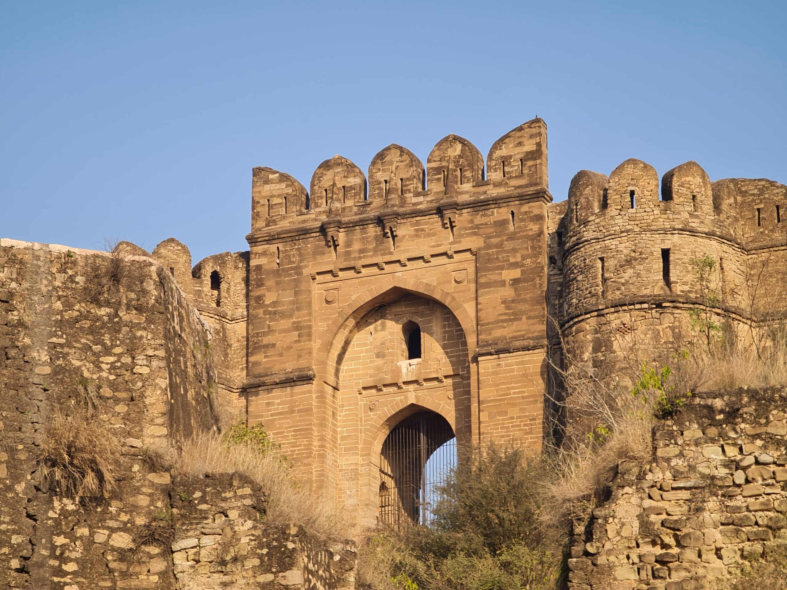 The arched sandstone gateway of Rohtas Fort at Jhelum, its crenellated walls rising above the surrounding stonework
