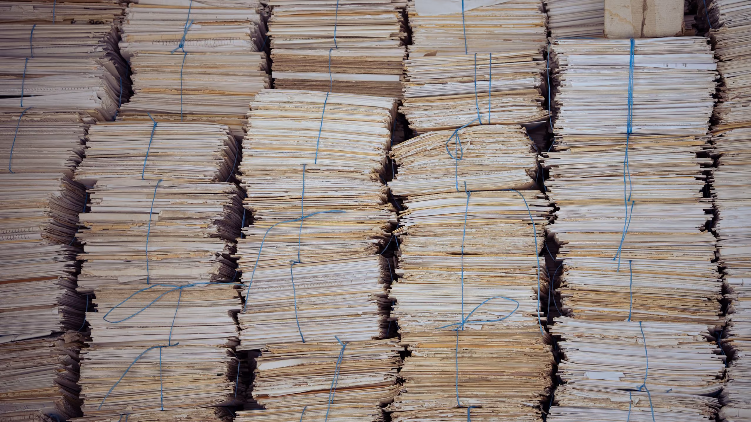 Tall stacks of paper files tied with string, bundled and piled one on top of another