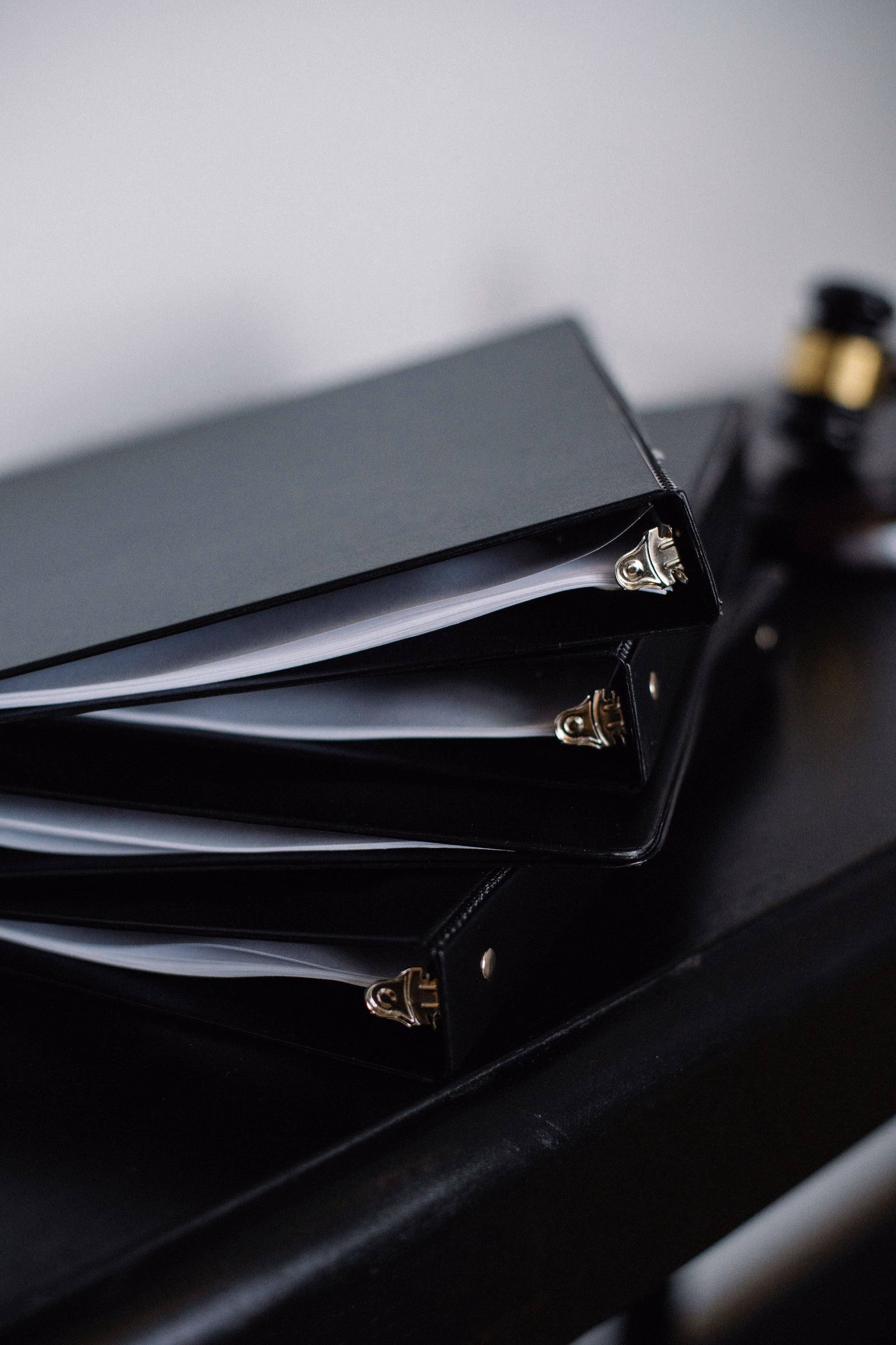 Black ring binders of documents stacked on a dark desk, a wooden gavel resting behind them