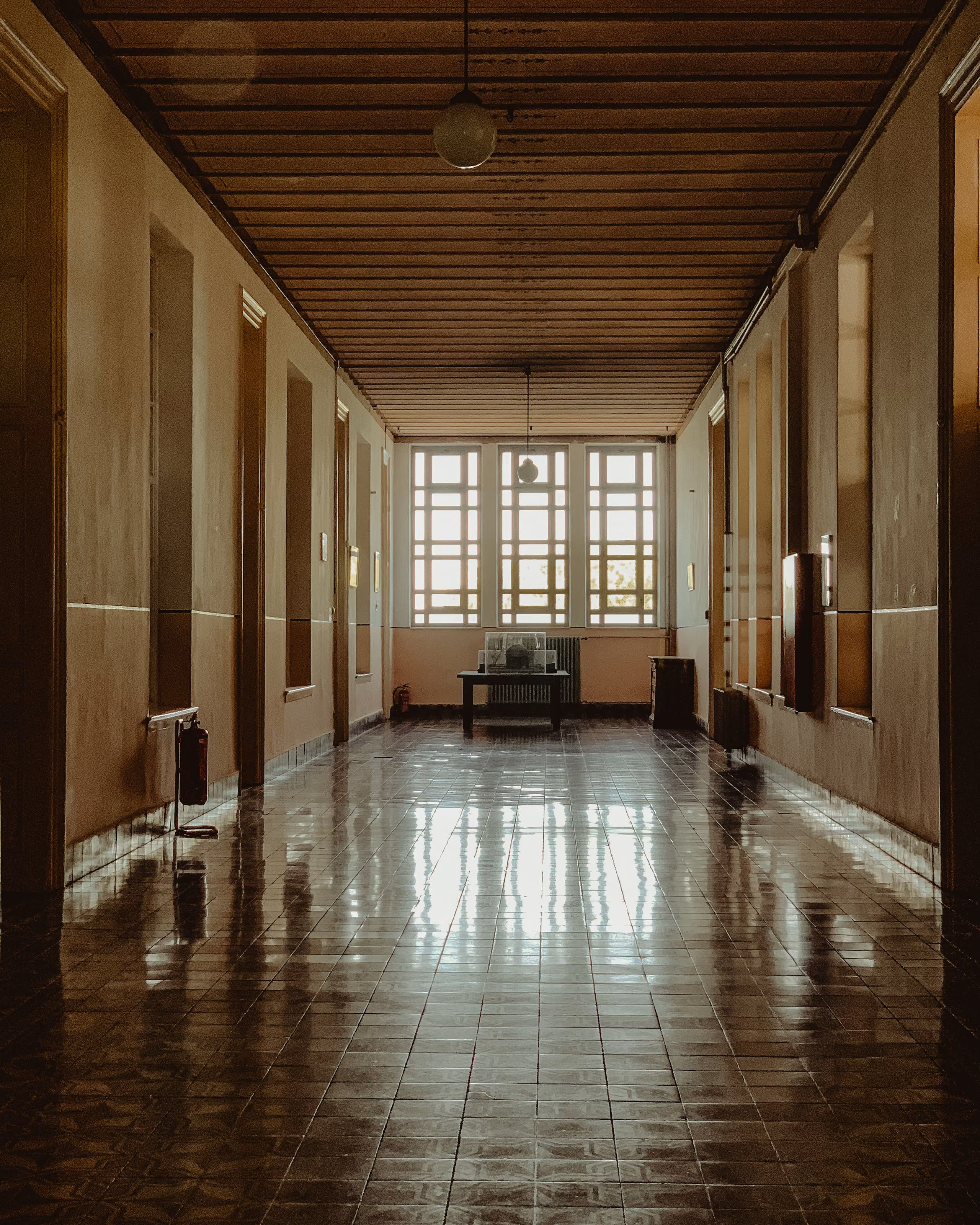An empty corridor in an old official building, daylight from tall windows reflecting off the tiled floor