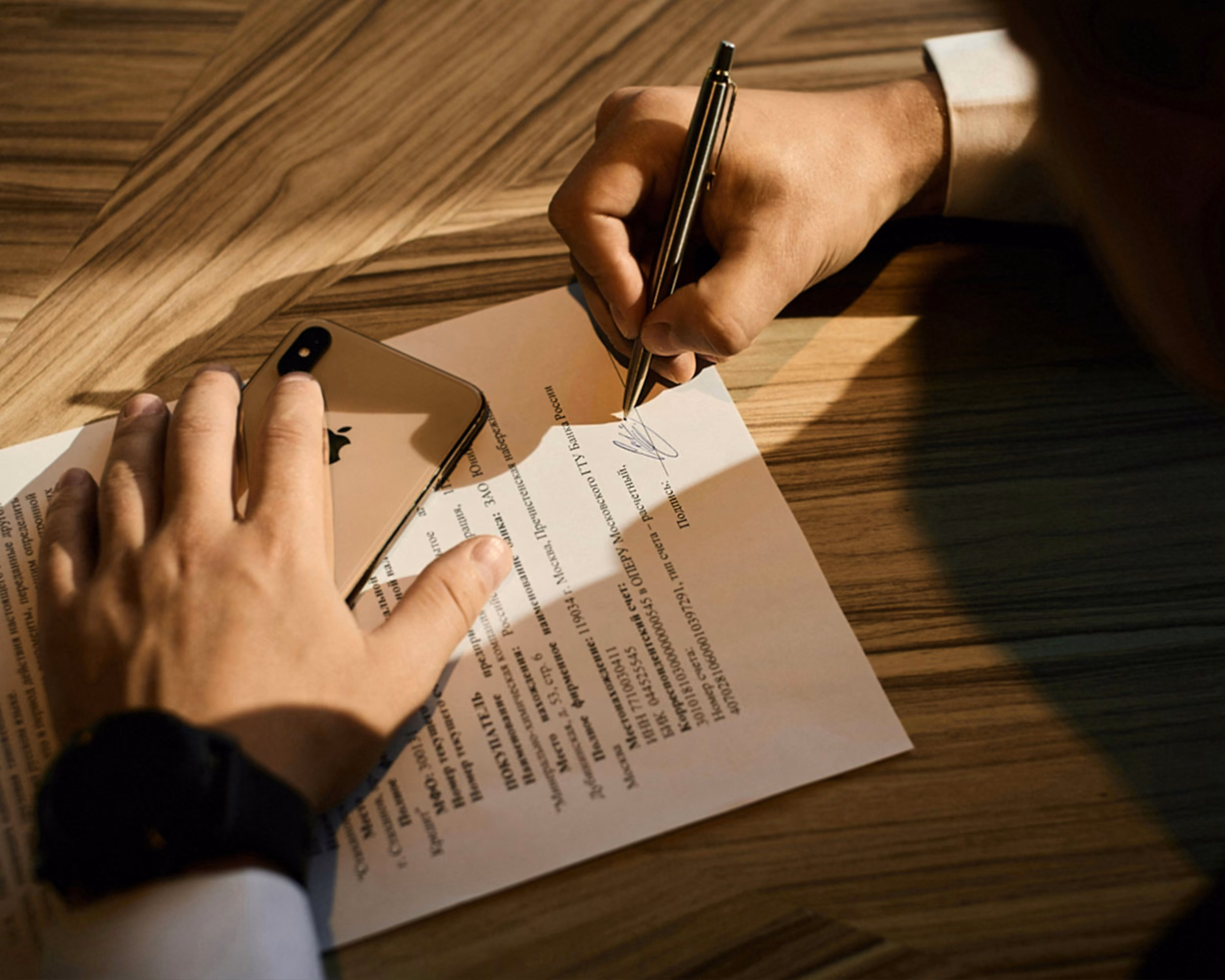 Close-up of a hand signing a printed document with a fountain pen on a wooden desk